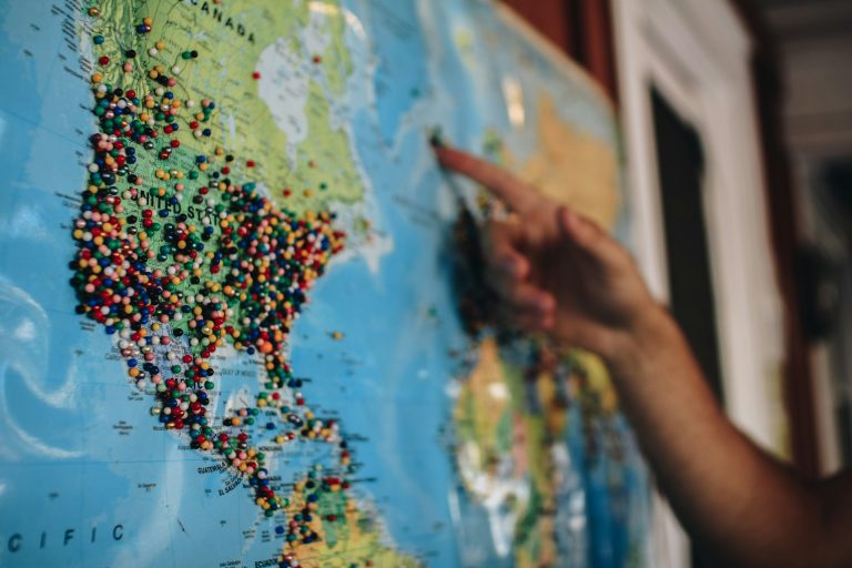 Personne pointant une carte du monde couverte d’épingles, symbole de la mobilité internationale