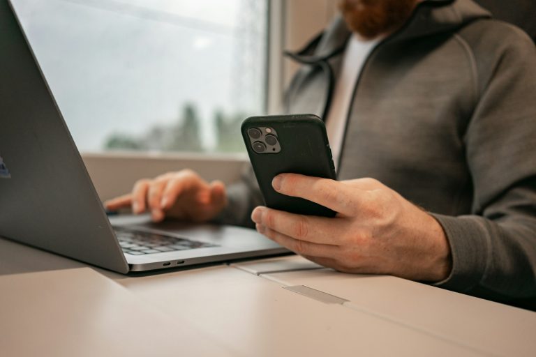 Homme connecté à un ordinateur portable, smartphone en main