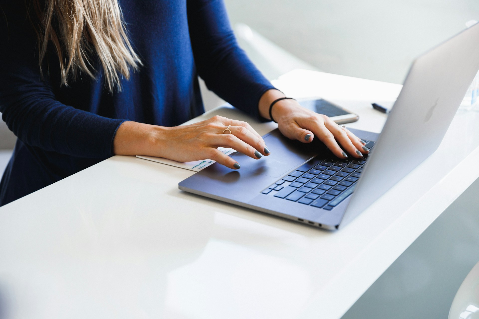 Personne tapant sur le clavier d’un ordinateur portable posé sur un bureau blanc